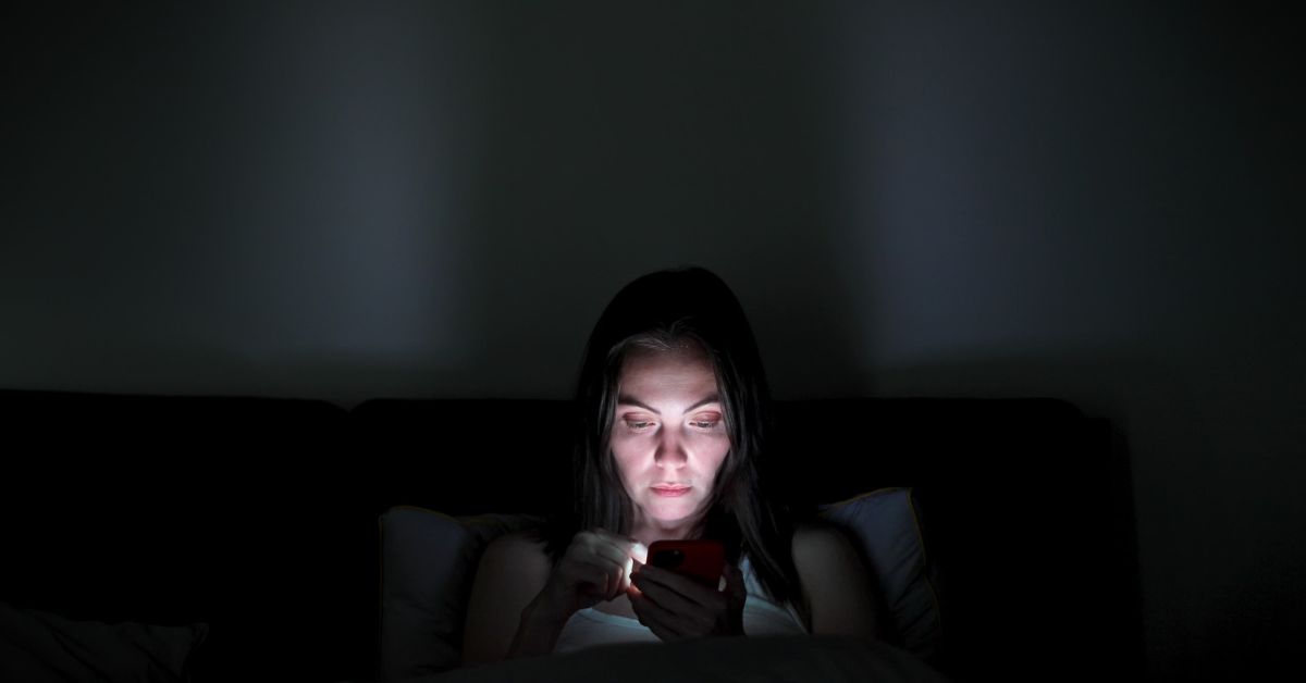 A woman combating addiction while browsing her phone in the dark.