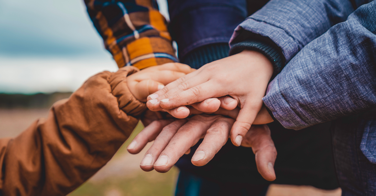 A group of hands holding each other in the middle of a field, symbolizing rebuilding relationships.