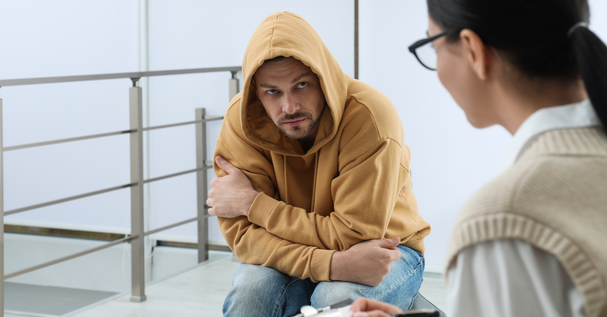 A man in a hoodie is taking the first step in recovery by talking to a woman.