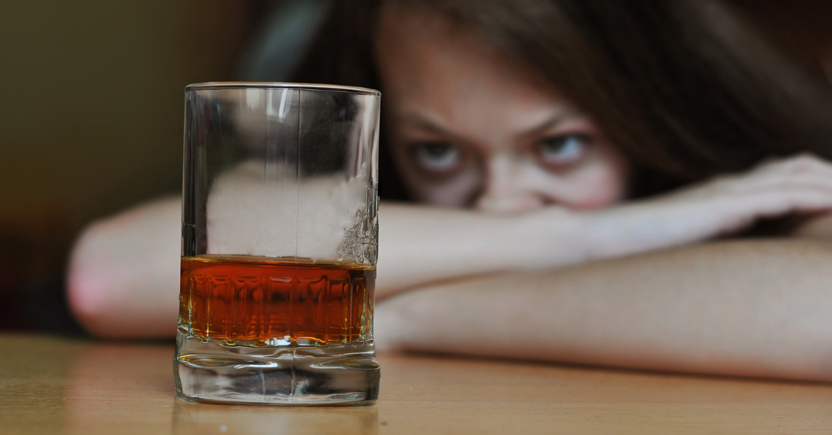 A woman exhibiting the 4 C's of addiction while leaning over a glass of whiskey.
