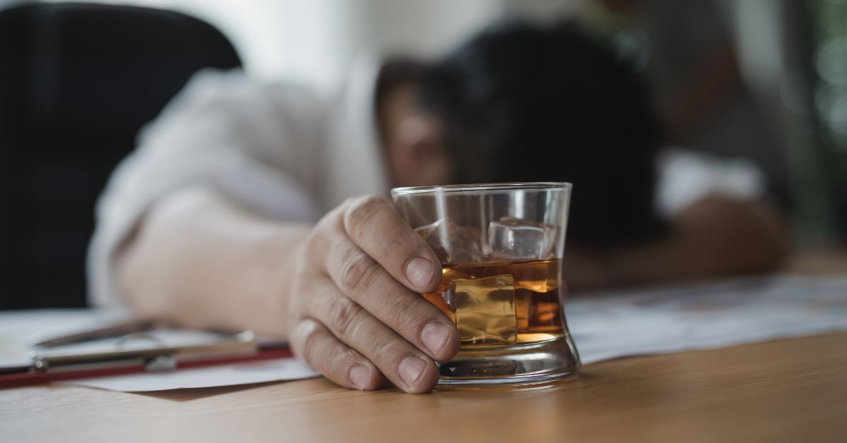 A man displaying alcohol addiction, which is often recognized as an illness, with a glass of whiskey on a desk.