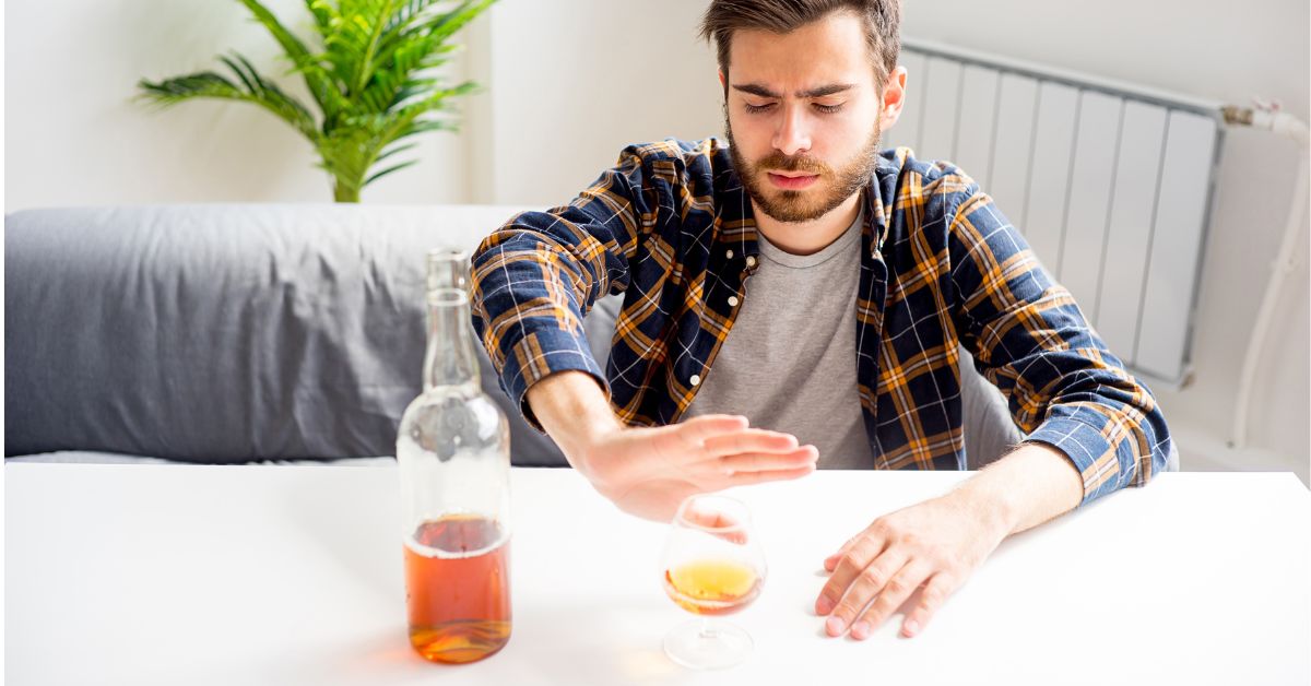 A man confronting alcoholism as a disease while sitting at a table with a glass of alcohol.