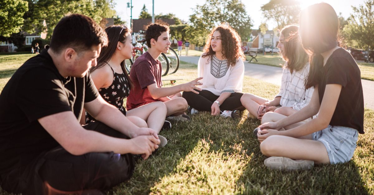 A group of young people talking about the importance of helping teen drug addicts and sitting in a circle on the grass.