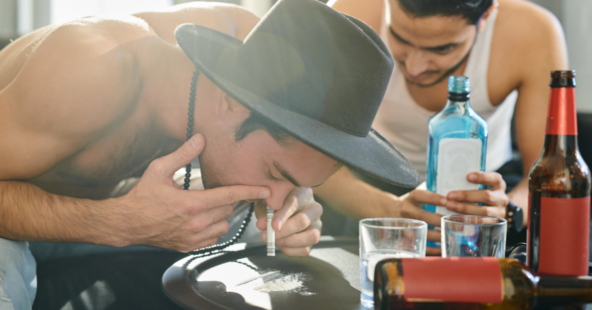 A man in a high-risk situation for relapse is smoking a cigarette while another man is drinking alcohol.