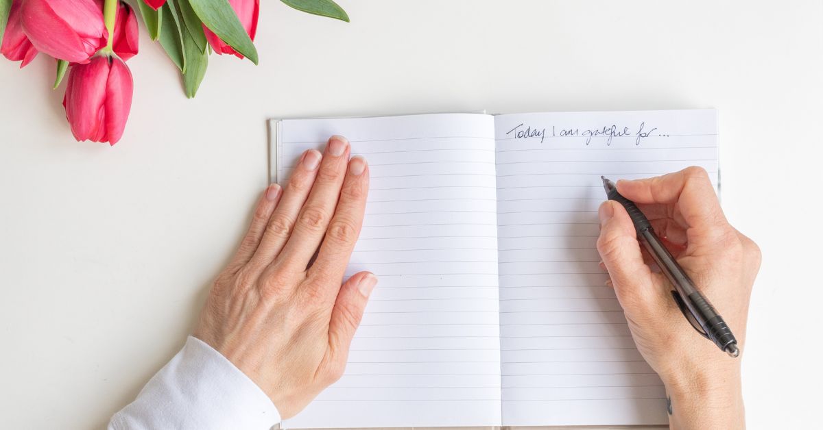 A woman writing her gratitude list in a notebook next to tulips.