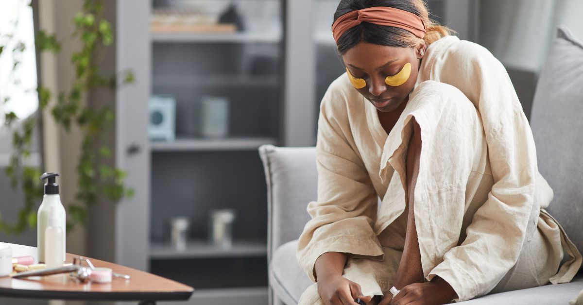 A woman practicing self care in a bathrobe sitting on a couch.