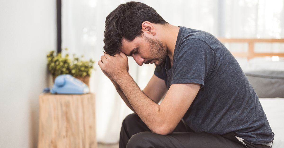 A man fighting relapse triggers sitting on a bed with his hand on his head.