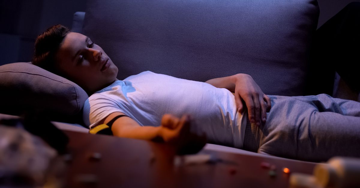 A young man experiencing the consequences of teen drug abuse while laying on a couch at night.