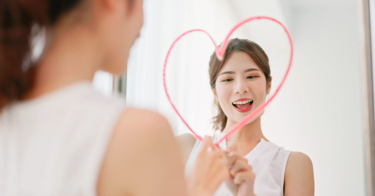 A woman is holding a heart shaped mirror in front of a mirror, reflecting self-esteem and recovery from addiction.