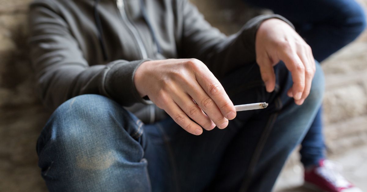 A young man sitting down with a cigarette in his hand, potentially showcasing drug use among teens.