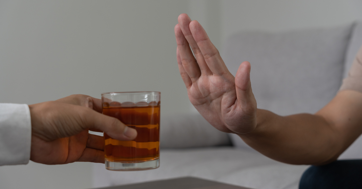 A man is handing a glass of alcohol to another man who is embracing sobriety.