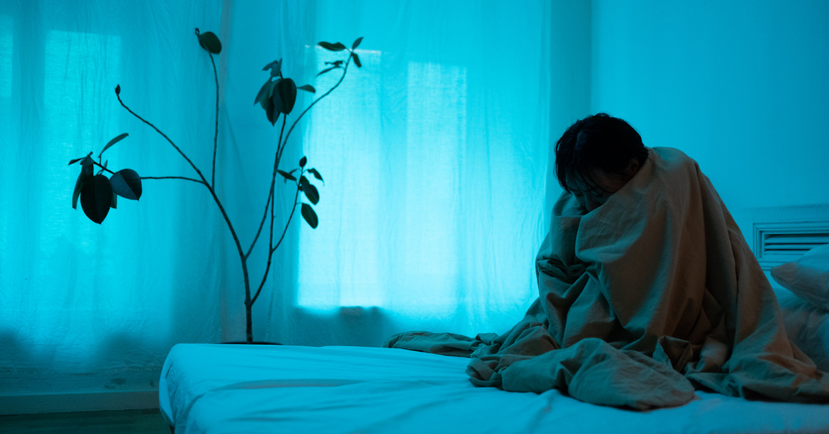 A person is wrapped in a blanket on a bed, reflecting on their journey of self sabotage in addiction recovery.