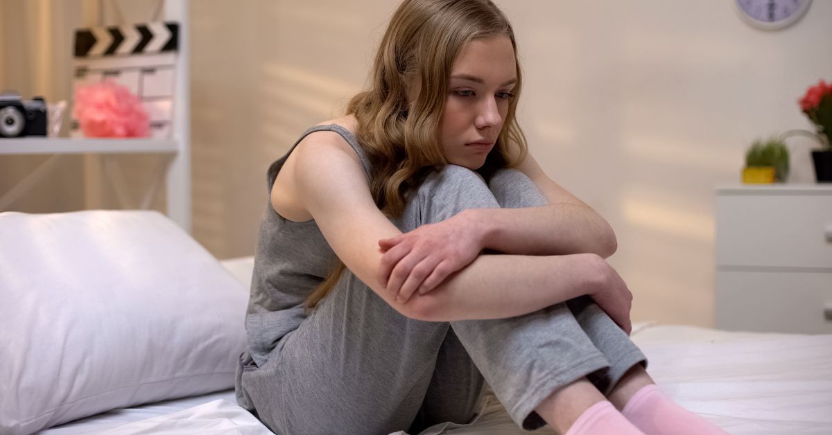 A young girl sitting on a bed with her hands on her knees, symbolizing serenity and reflecting the challenges of early sobriety.