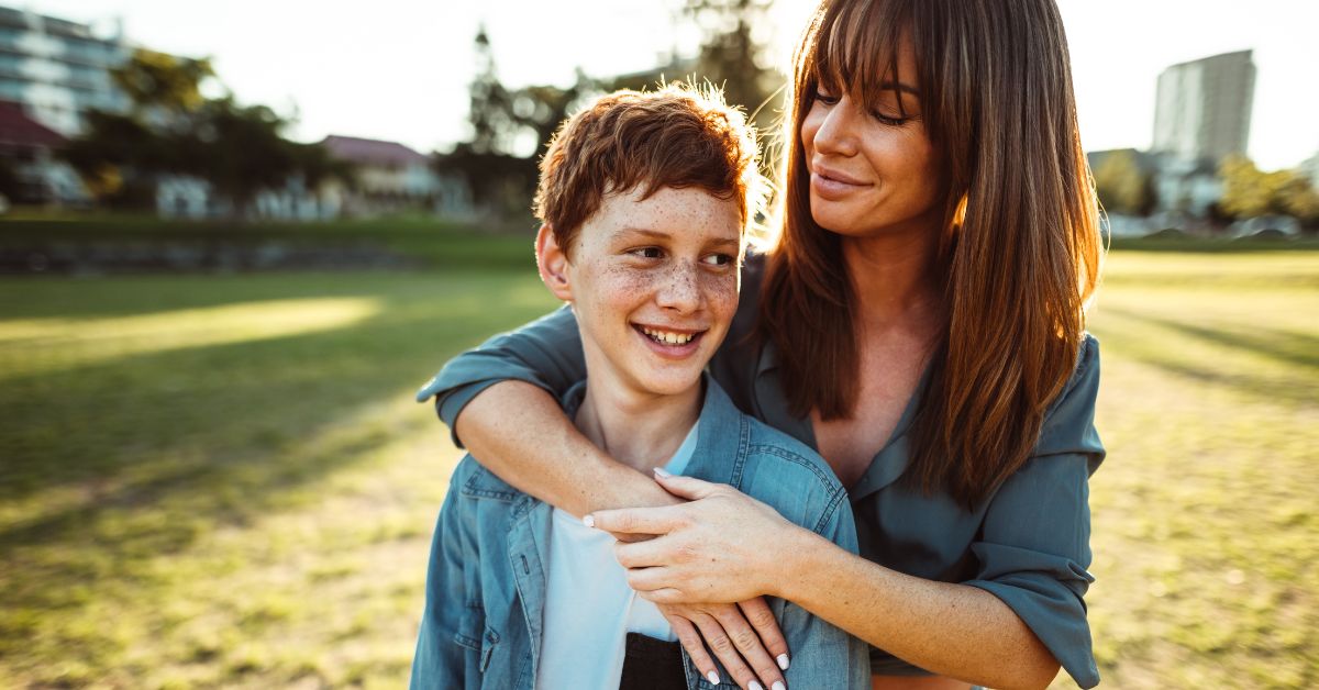 A woman tightly embracing her son in a park, providing healing through their powerful bond of love and nurturing his empowerment.