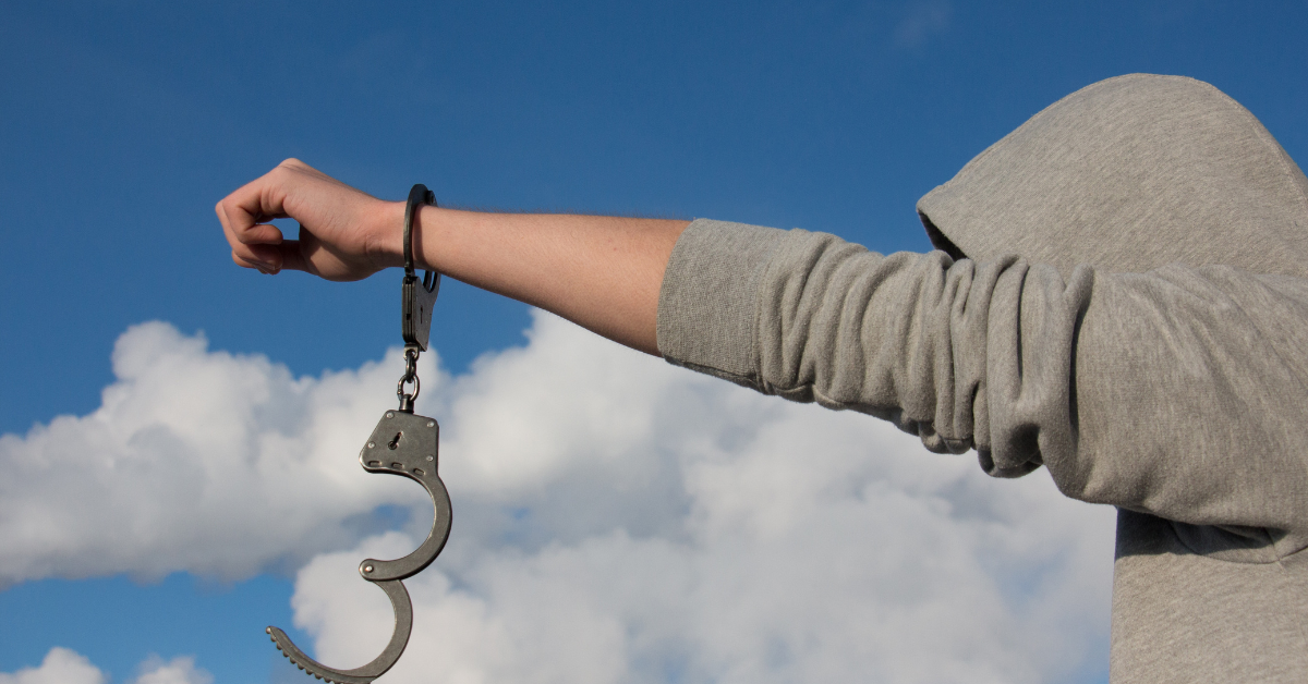 A man holding a pair of handcuffs against a blue sky, symbolizing freedom through sobriety.
