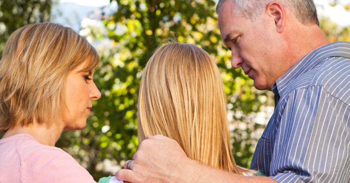 A man, a woman, and a girl engage in prevention strategies for drug abuse while hugging in a park.