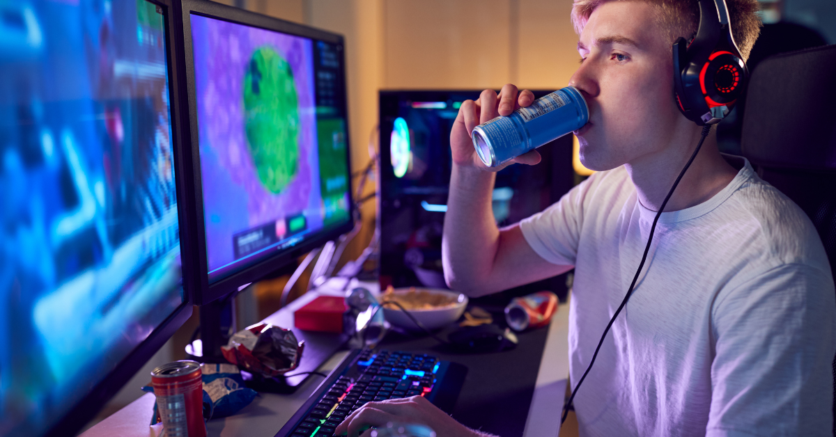A teenager drinking from a bottle in front of two monitors.