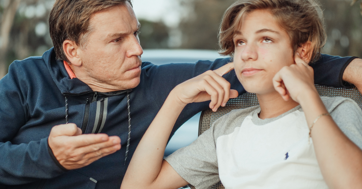 A father is engaging in a conversation with a boy sitting on a bench, discussing why adolescence is a crucial time to prevent drug abuse.