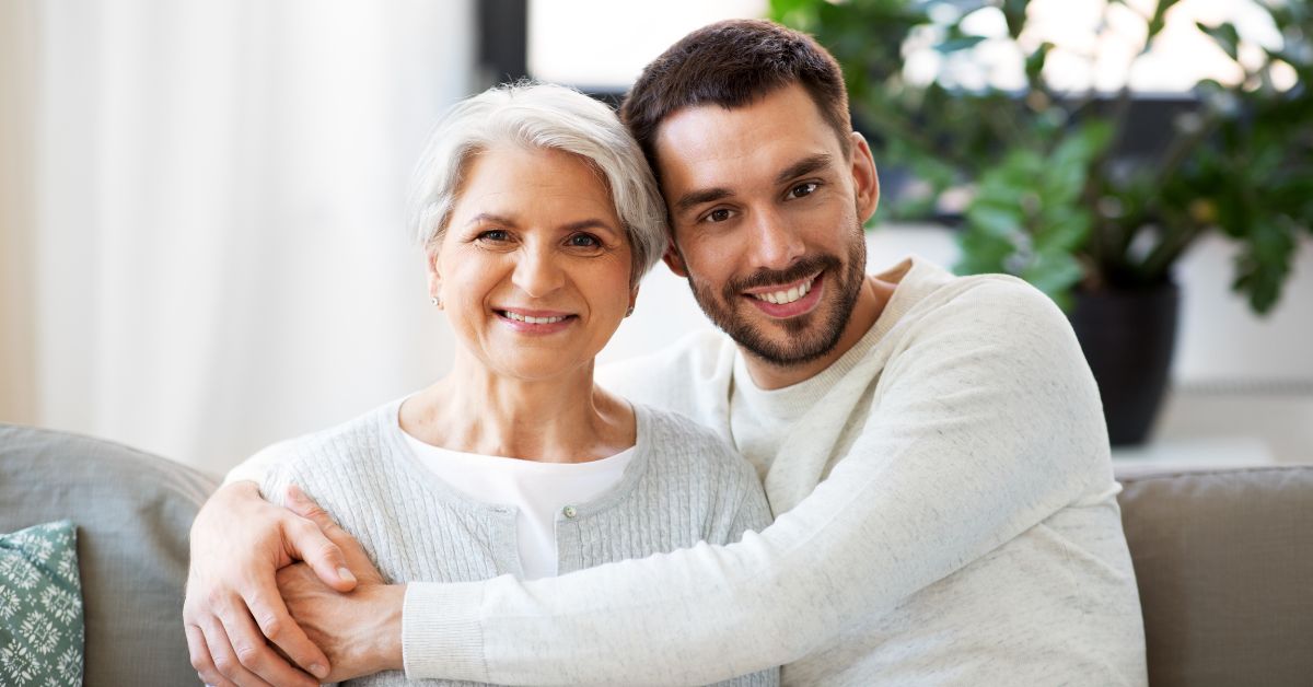 A man and his mother cultivating a free lifestyle by hugging affectionately while sitting on a couch.