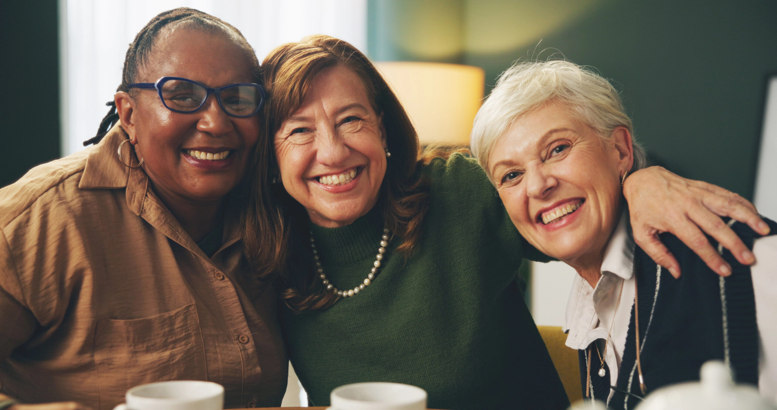 Three mature women embracing and laughing at a kitchen table