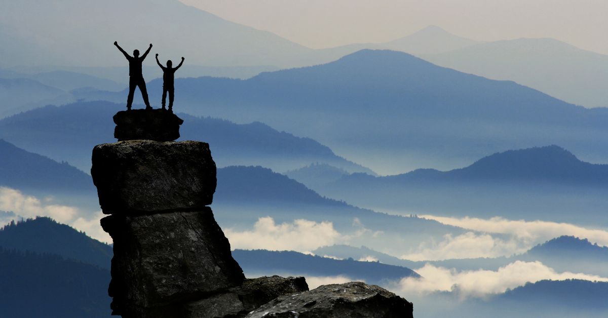 Two people standing on top of a mountain, having successfully broken free from codependency and alcohol addiction.