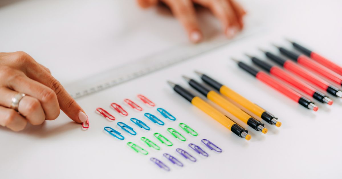 A woman's hand obsessively holding pens and pencils on a white table.