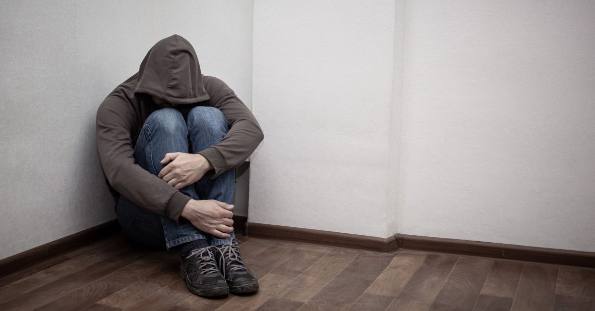 A man in a hoodie struggling on the floor in an empty room, depicting a compassionate approach towards helping an addict in denial.