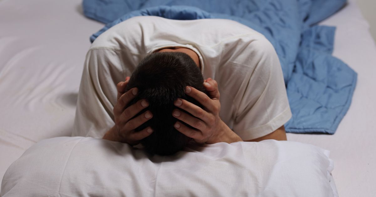 An emotionally unavailable man, possibly an alcoholic, laying on a bed with his head on his pillow.