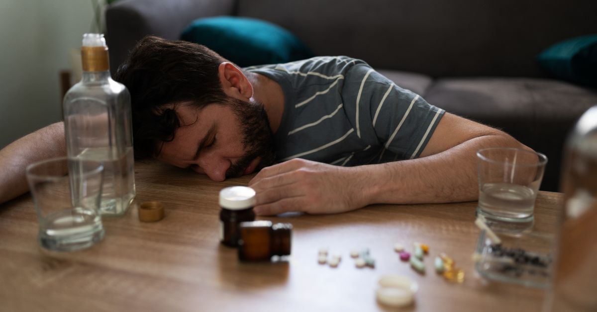 Early warning signs of relapse: A man sleeping on a table surrounded by bottles and pills.