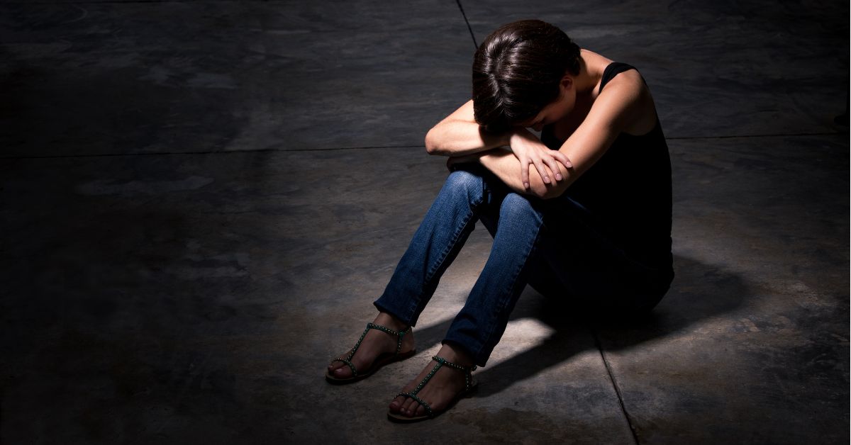 A woman with her hands on her knees, displaying the effects of low self-esteem in recovery.
