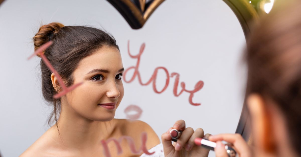 A girl is practicing self-forgiveness by writing "I love me" on a mirror.