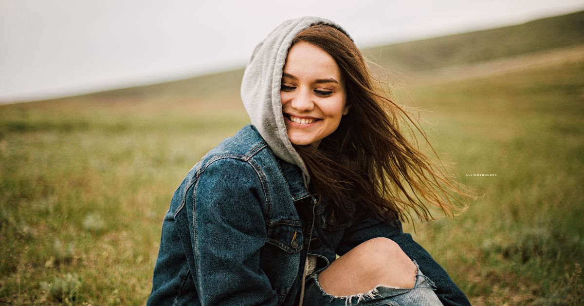 A young woman, embracing sobriety, holistic healing, and recovery, wearing a hoodie as she sits in a field.