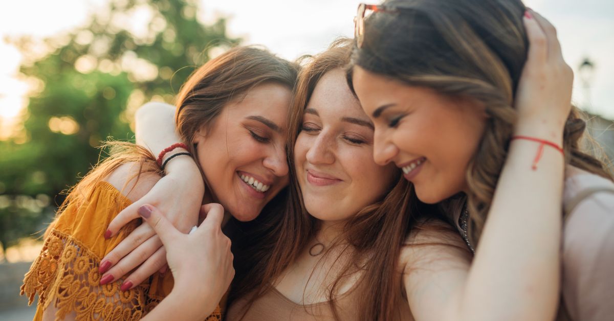 Three women hugging each other, ending the vicious cycle, and smiling at the camera.