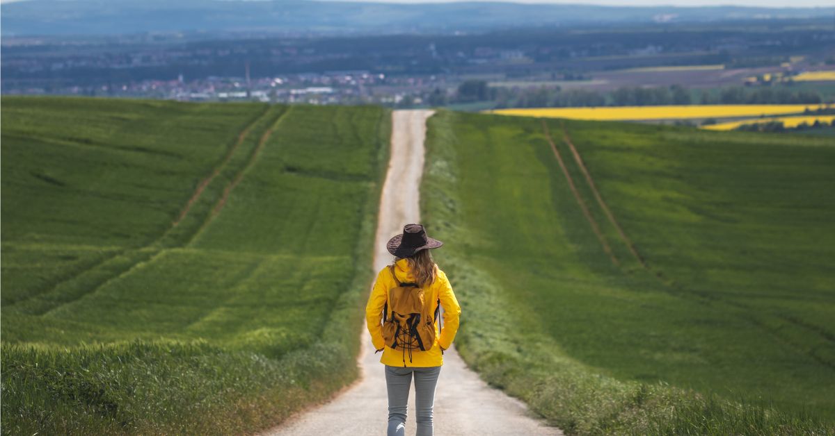 A woman on a journey to addiction recovery walking down a dirt road in a yellow hoodie.