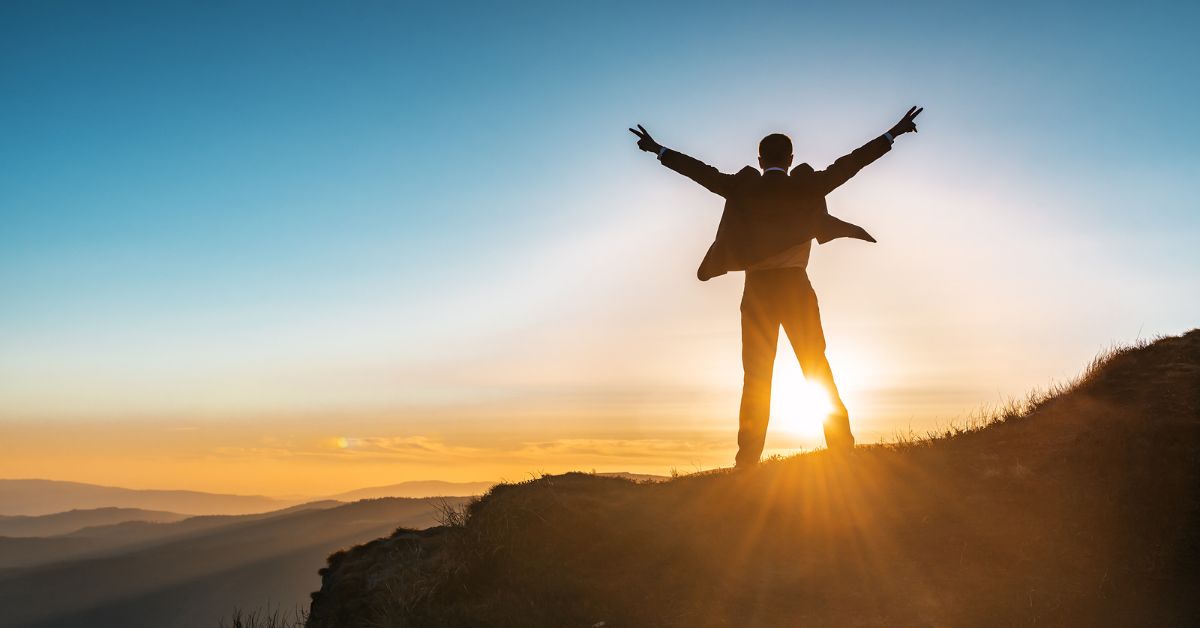 A person maintaining accountability while standing on top of a mountain with his arms raised.