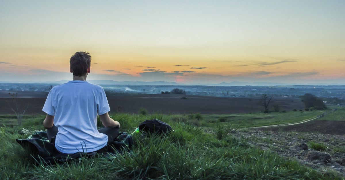 A man engaging in healthy coping skills while sitting in a field at sunset.