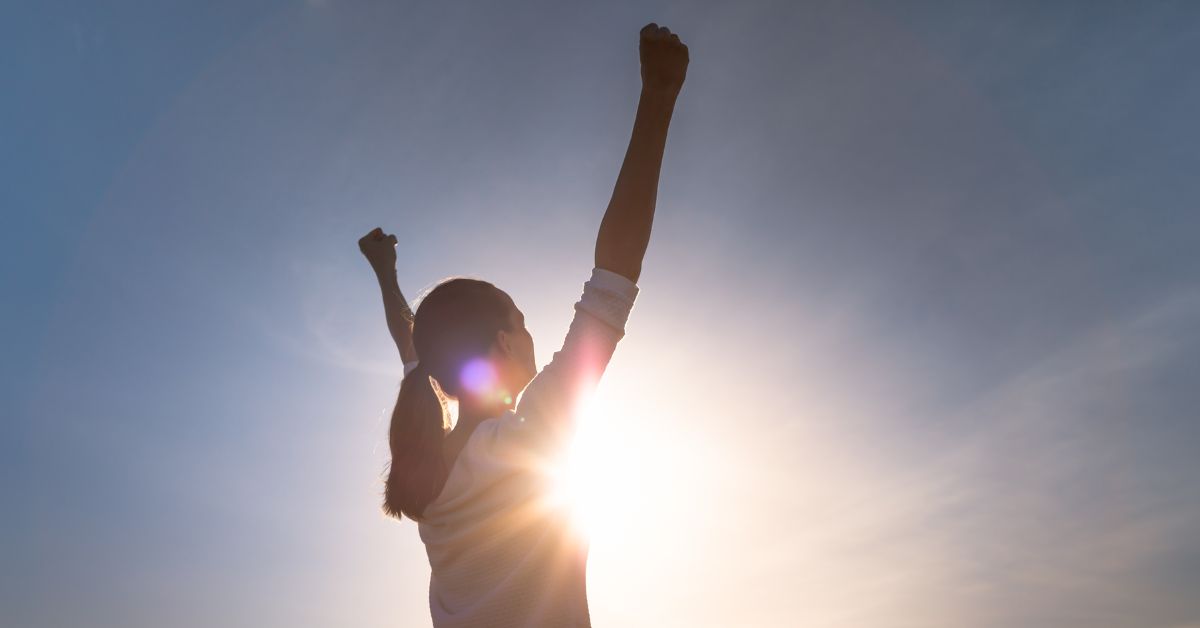 A woman with her arms raised in the air overcoming addiction.