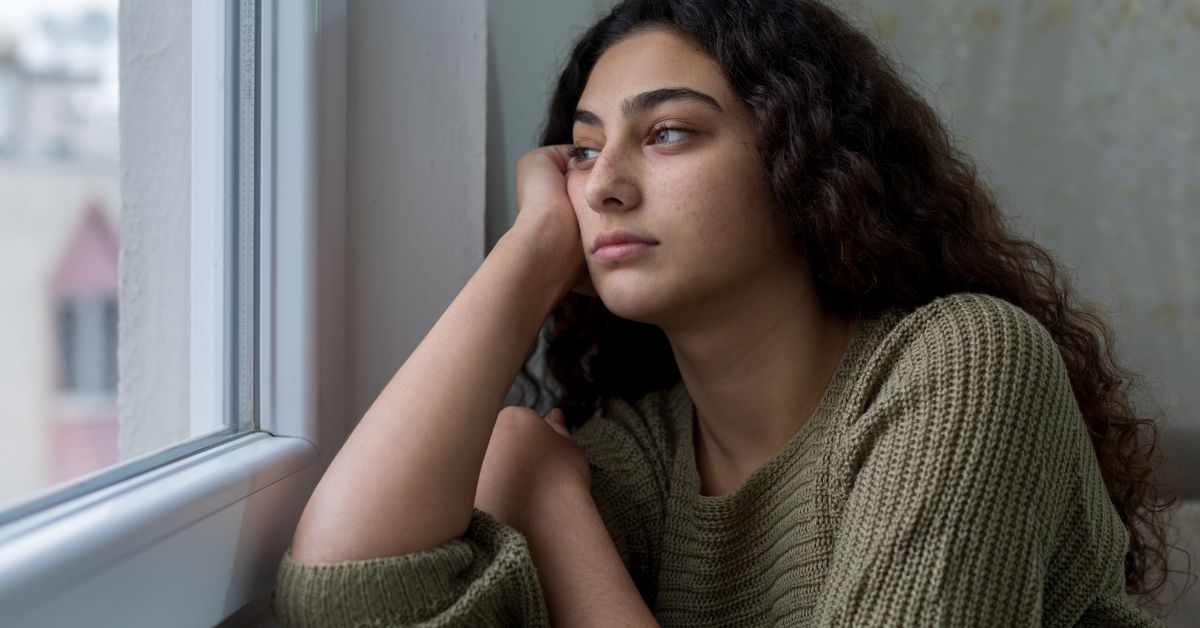 A young woman navigating early challenges in recovery while looking out of a window.