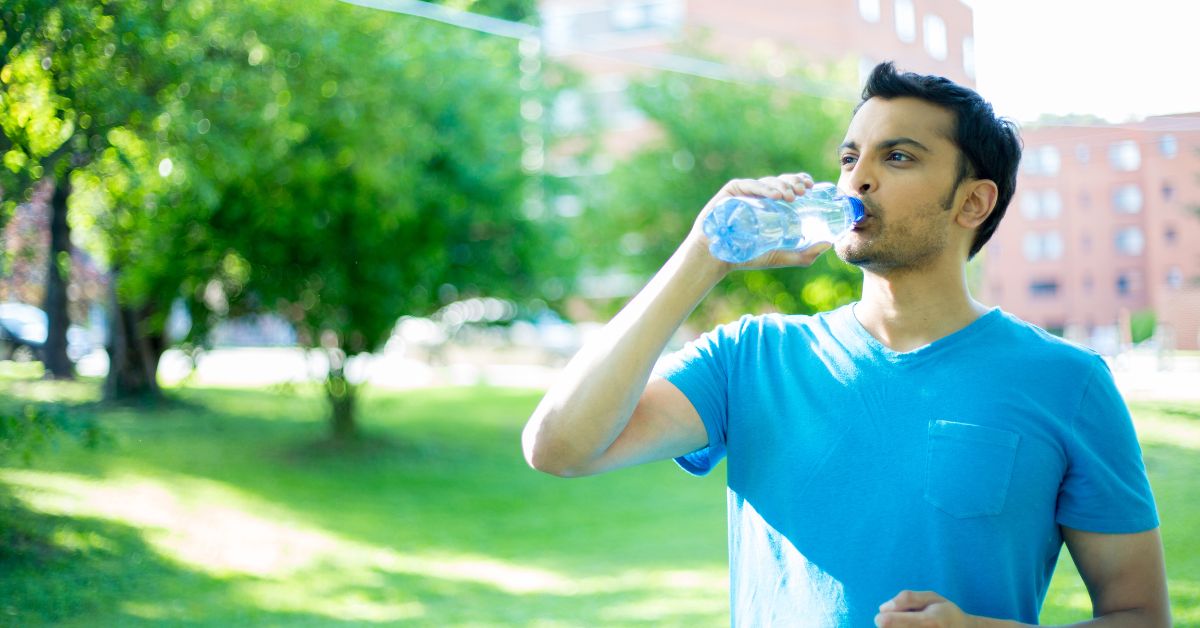 A man overcoming sobriety fatigue, drinks water from a bottle in a park.