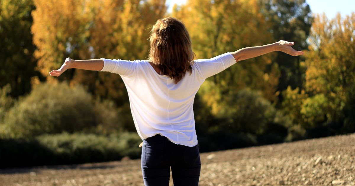 A woman standing in a field with her arms outstretched after overcoming crack withdrawal symptoms. 