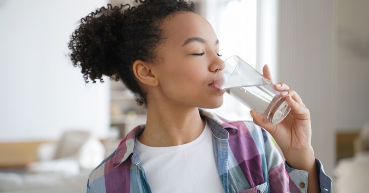 A young woman demonstrating commitment to sobriety while drinking water from a glass. 