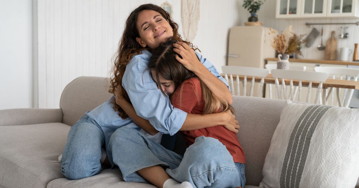 Two women hugging on a couch in a living room, demonstrating the importance of sober living and support.