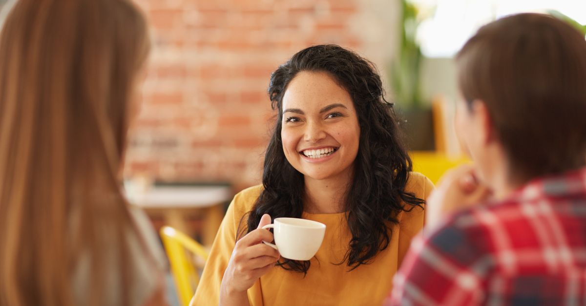 A group of women sitting around a table and supporting each other in their addiction treatment journey while enjoying a cup of coffee.