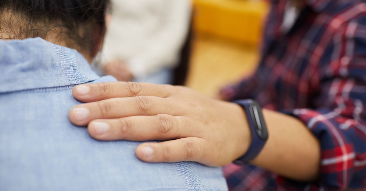 A woman is providing support to a child's hand in front of a group of people.