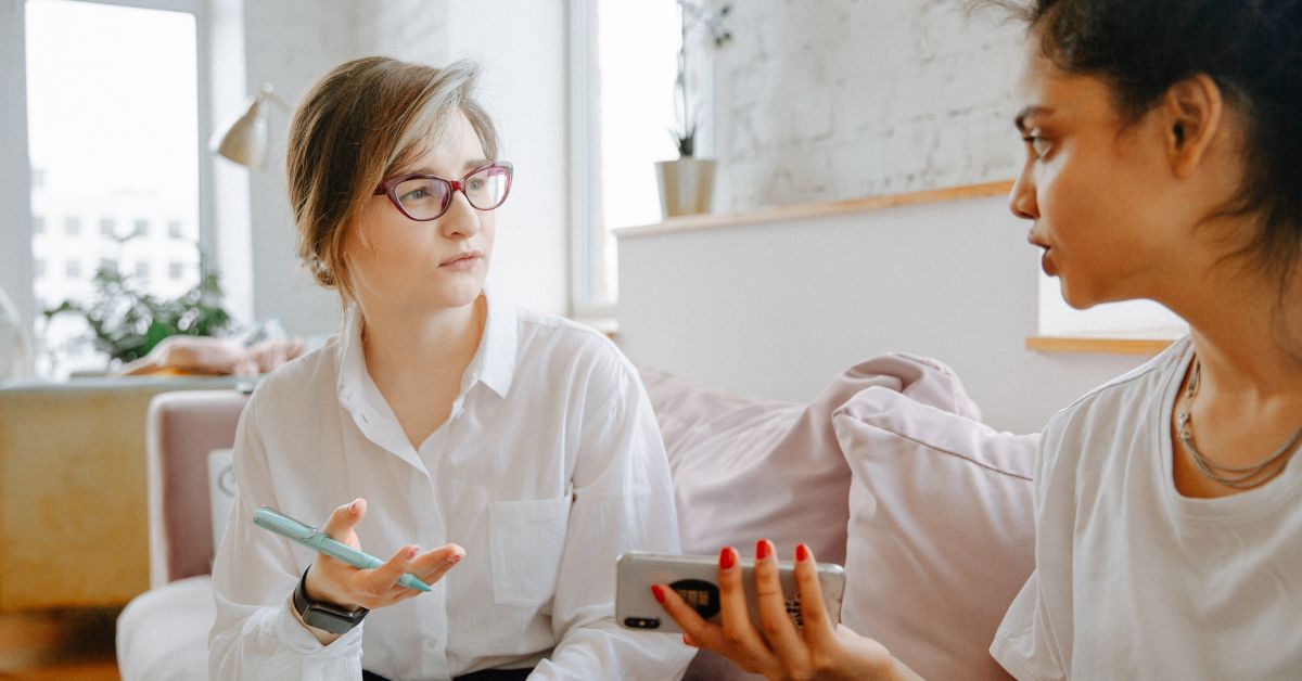 Two women sitting on a couch engaging in a deep conversation about the first step to stop self sabotage.