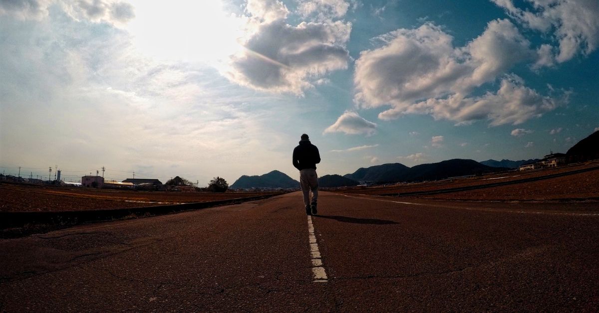 A man is standing on a road with mountains in the background thinking about the road to recovery.