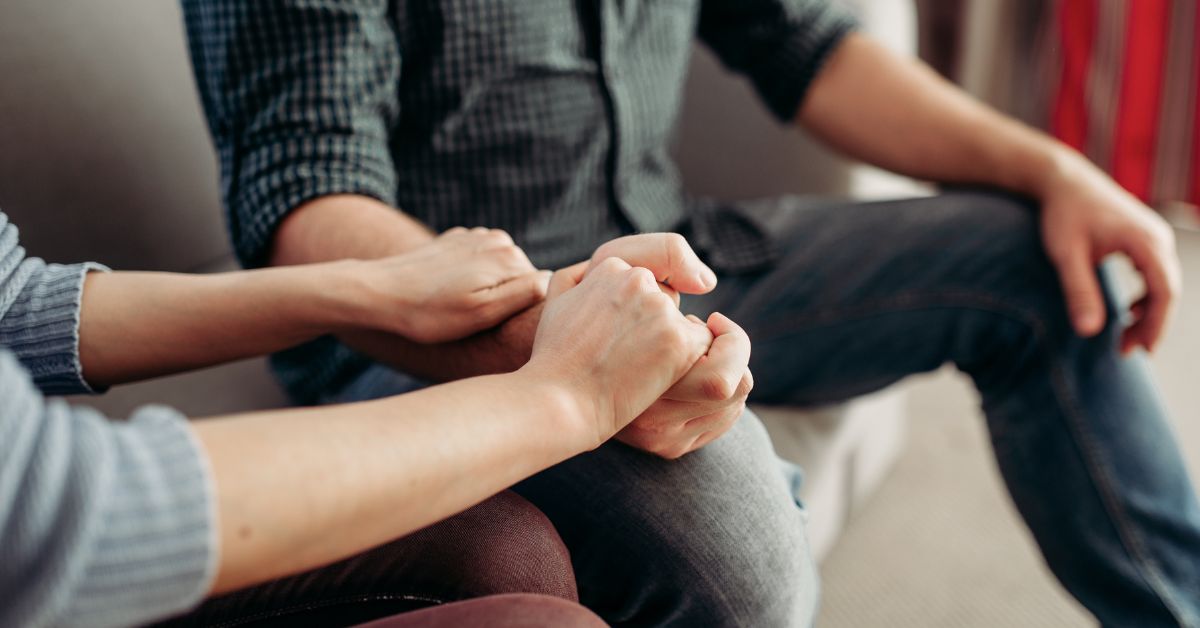 Two people sitting on a couch, seeking the road to get help for addictive personality while holding hands.