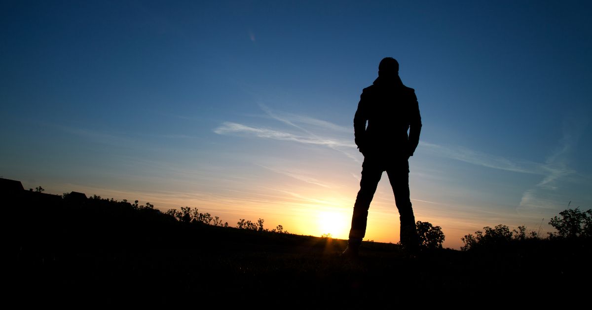 A silhouette of a man overcoming addiction recovery in a field at sunset.