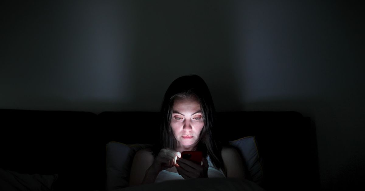 A woman combating addiction while browsing her phone in the dark.	