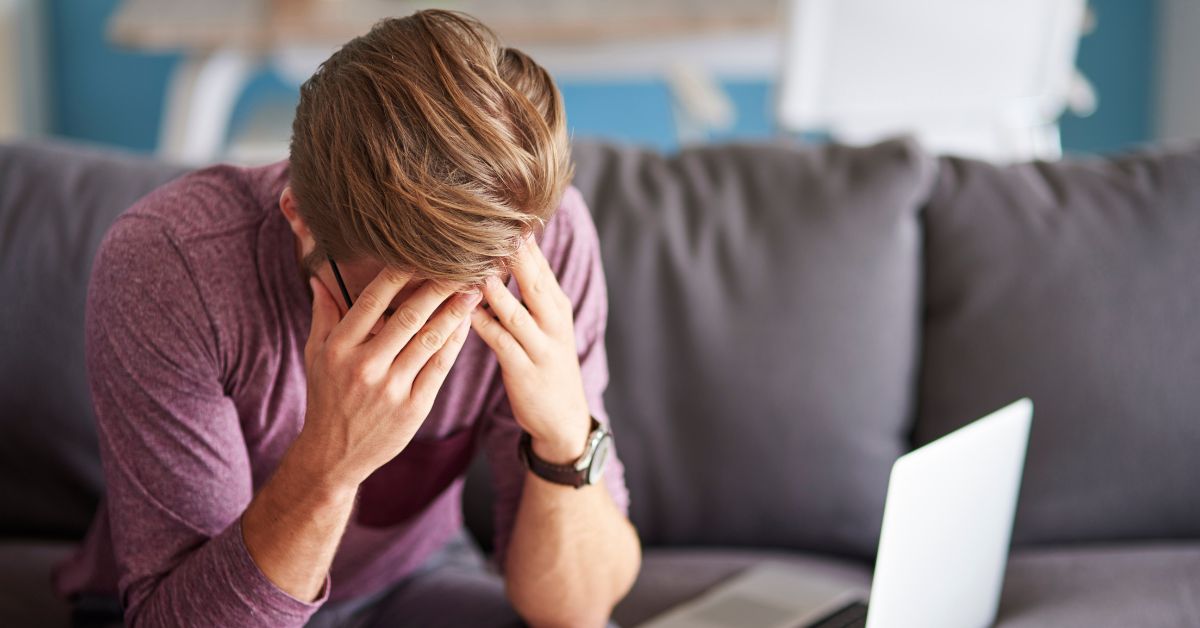 A man is exhibiting stages of relapse while sitting on a couch with his hands on his face.